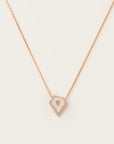 lose-up of a rose gold necklace featuring a geometric pendant with mother of pearl center, surrounded by a halo of pavé diamonds.