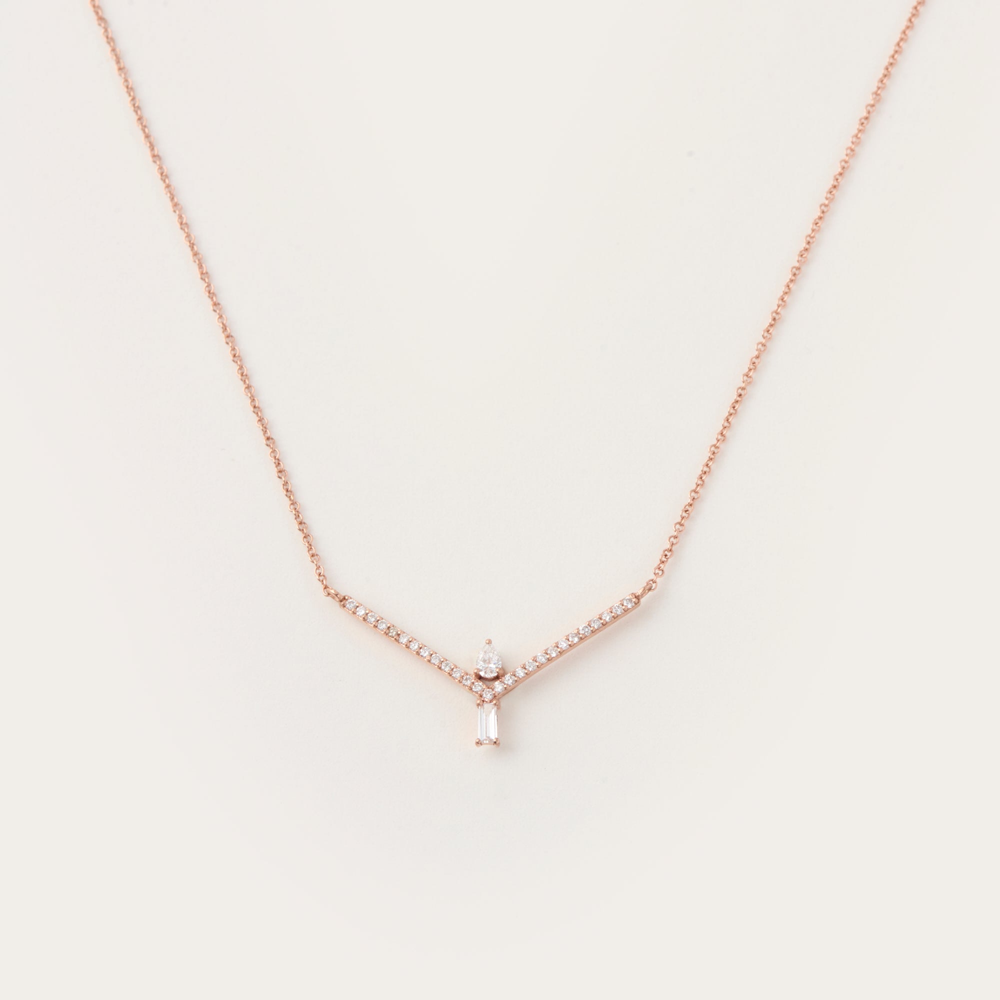 Delicate rose gold necklace featuring a V-shaped diamond-accented frame with a pear-cut diamond and a baguette-cut diamond pendant.