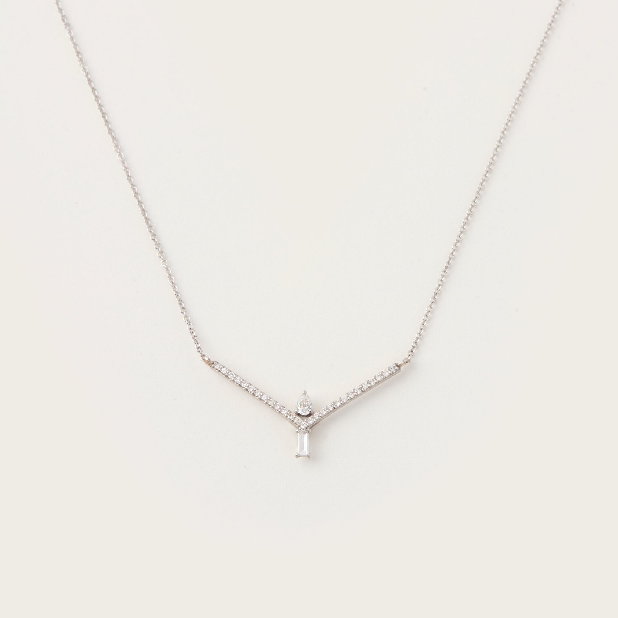 Elegant white gold necklace featuring a V-shaped diamond-accented frame with a pear-cut diamond and a baguette-cut diamond pendant.