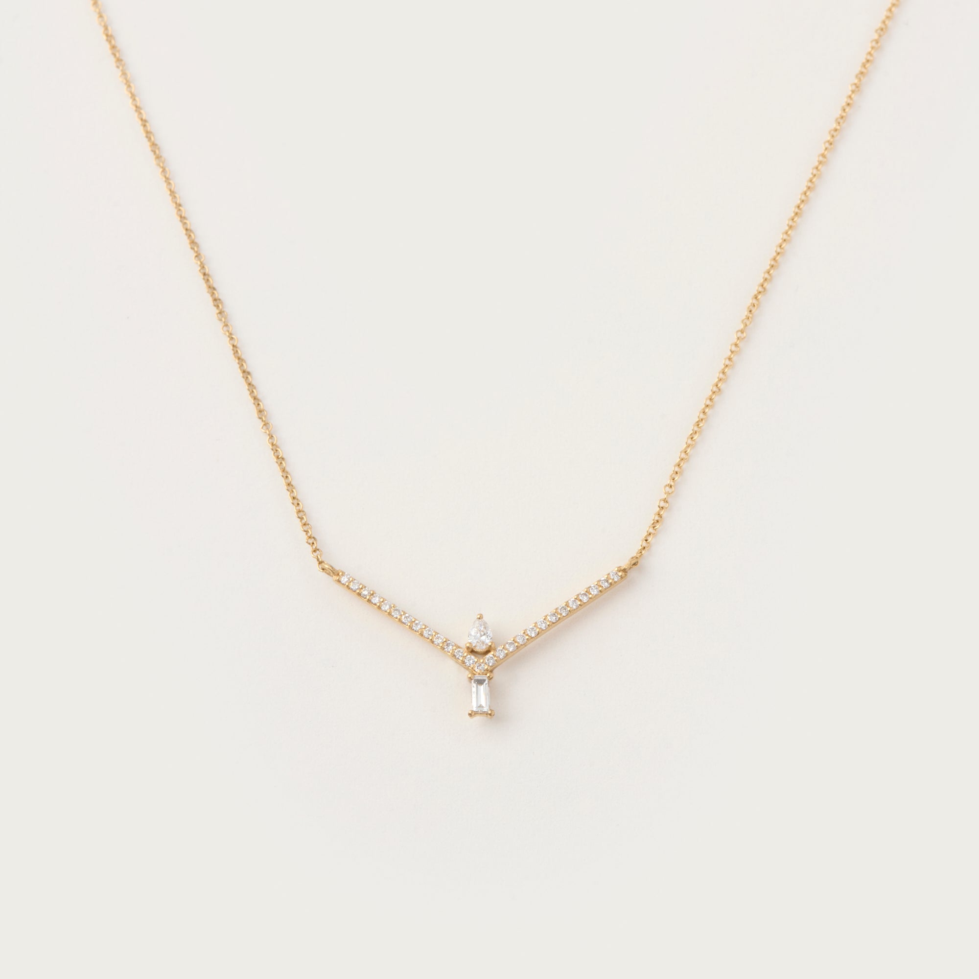 Sophisticated white gold necklace with a V-shaped diamond-accented frame, featuring a pear-cut diamond and a baguette-cut diamond pendant.